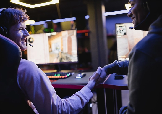 Two gamers wearing headsets shaking hands after a competitive gaming match.